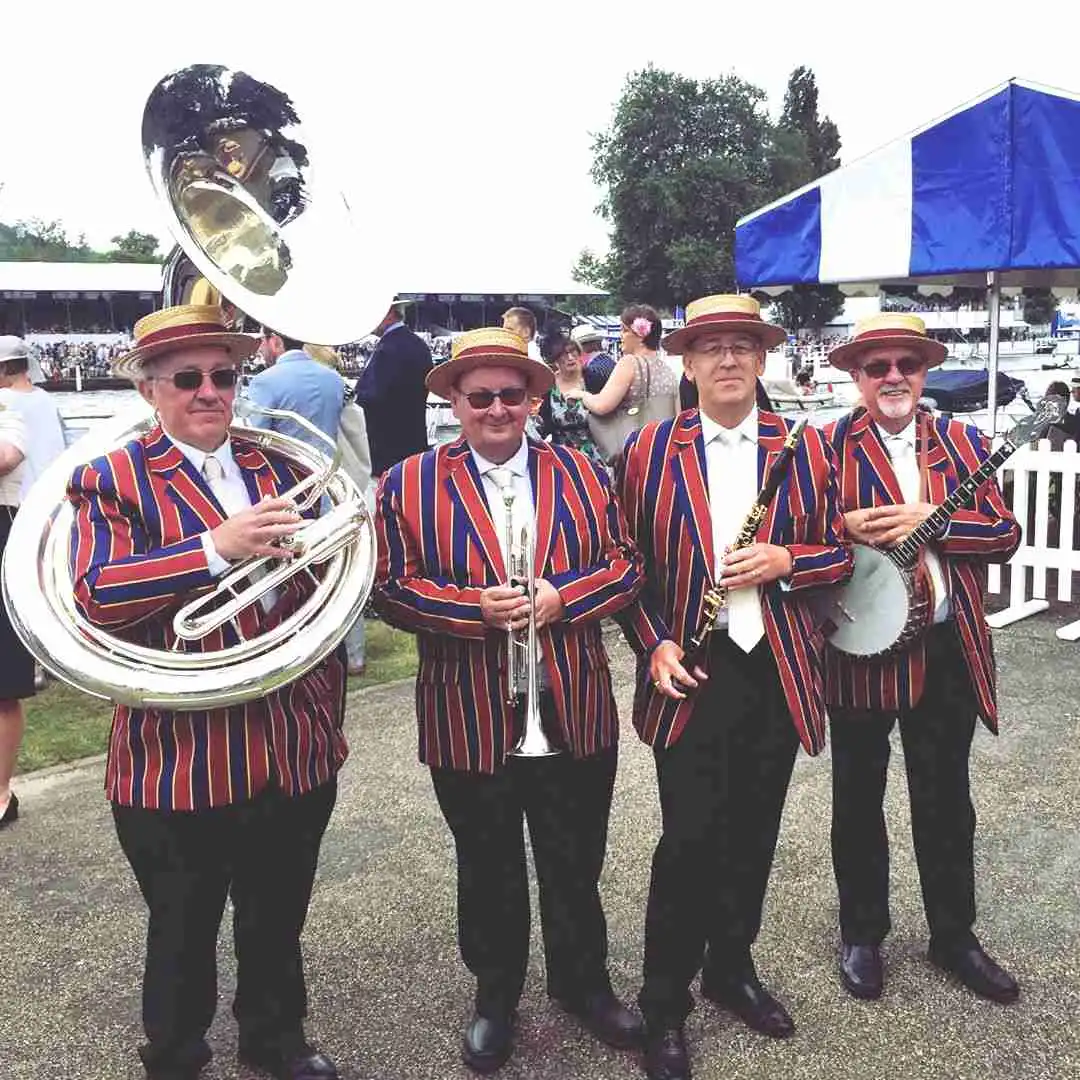jazz band, 4 men stood by the river with their instruments wearing red and blue blazers