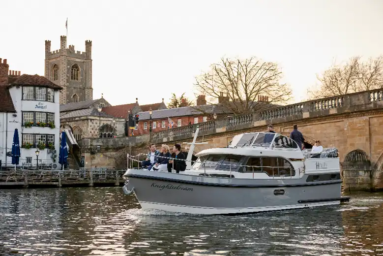 Hobbs of Henley boat Knightsdream cruising along the river thames with the famous Angel pub in the background. There are 3 passengers at the front of the boat, and 3 at the rear plus a skipper.