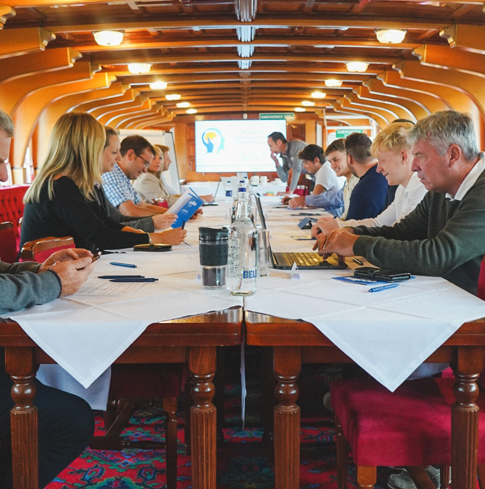 12 people sat around tables inside one of the Hobbs of Henley boats, set up with white table cloths, pens, glass water bottles and a TV screen for presenting.