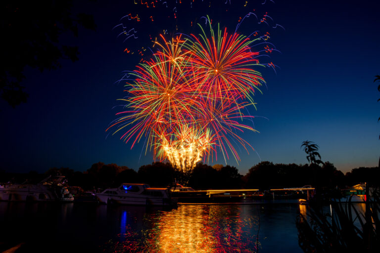 Brightly coloured fireworks at Henley Festival. Boats are lining the river thames at night.